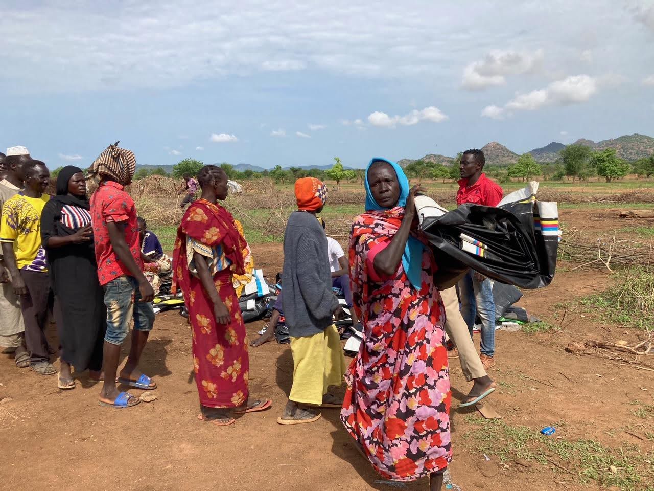 Sudanese woman carries Meadow billboard tarp and line of people receive billboard tarps