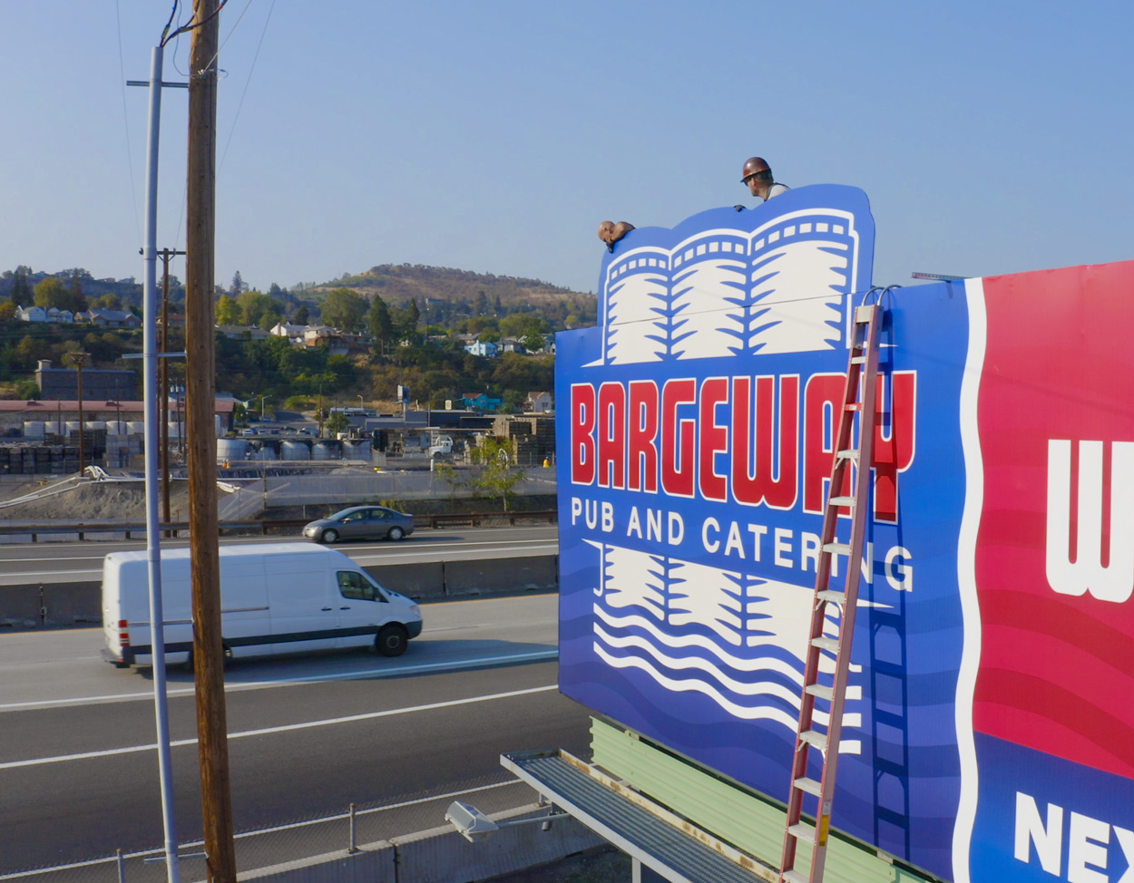 Crew working on putting up a blue and red billboard extension next to a freeway